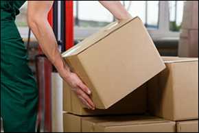 Two arms hold a moving box, putting it on stop of a stack of brown moving boxes.