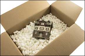 Packing box filled with packing peanuts and a small house on top.
