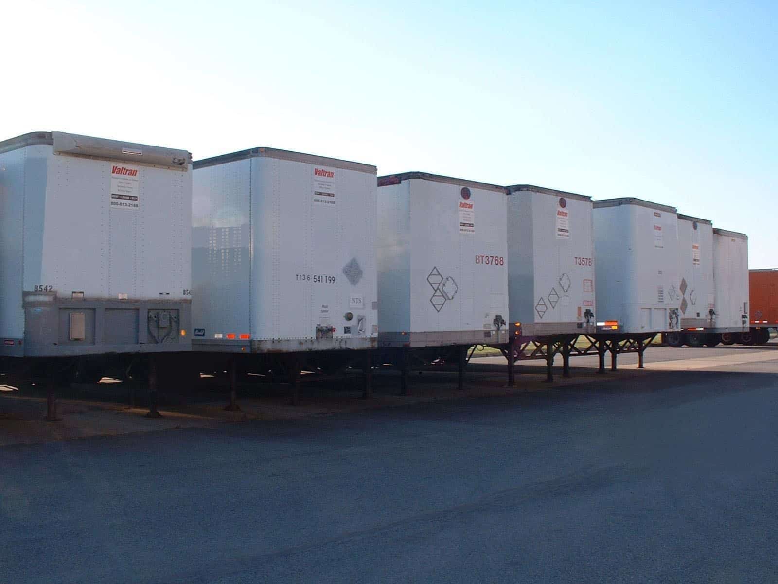 Four white storage trailers lined up in a row on black asphalt.