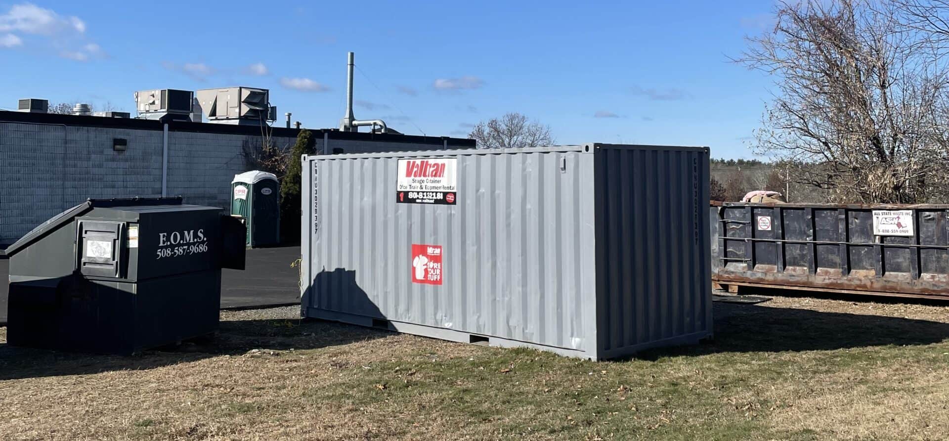 A Valtran storage container placed conveniently at the back of an office building near dumpsters and a portable toilet, representing its use for business storage needs.