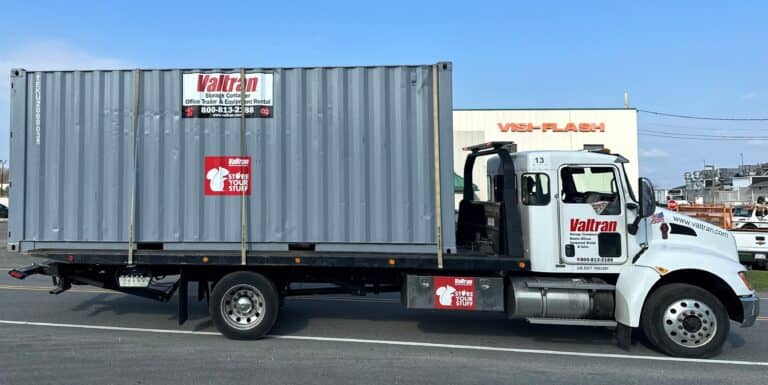 A grey Valtran portable storage container on a flatbed truck for an easy relocation.